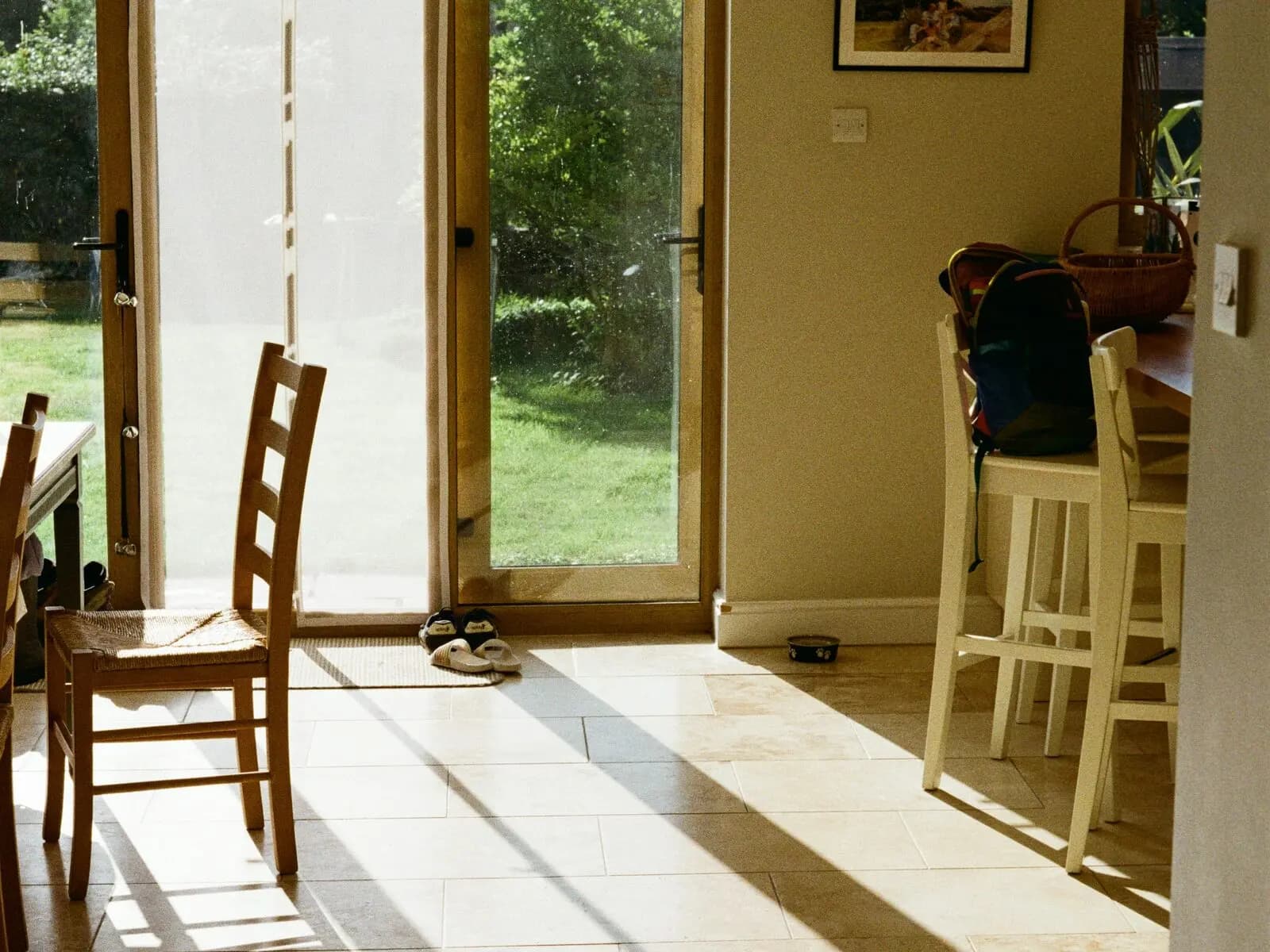 Morning light across the tiled floor of a family kitchen, garden doors open